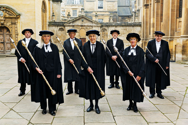 Seven robed officials each holding a metallic ceremonial staff
