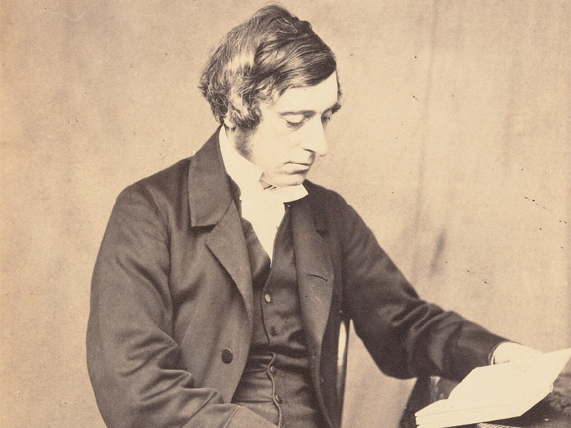 A black and white photograph of a man wearing a jacket and reading at a desk