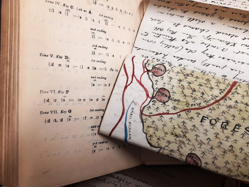 An open book showing tonic sol-fa type on the left page with a folded, hand-drawn map of a forest and a hand-written letter covering the right page of the book.