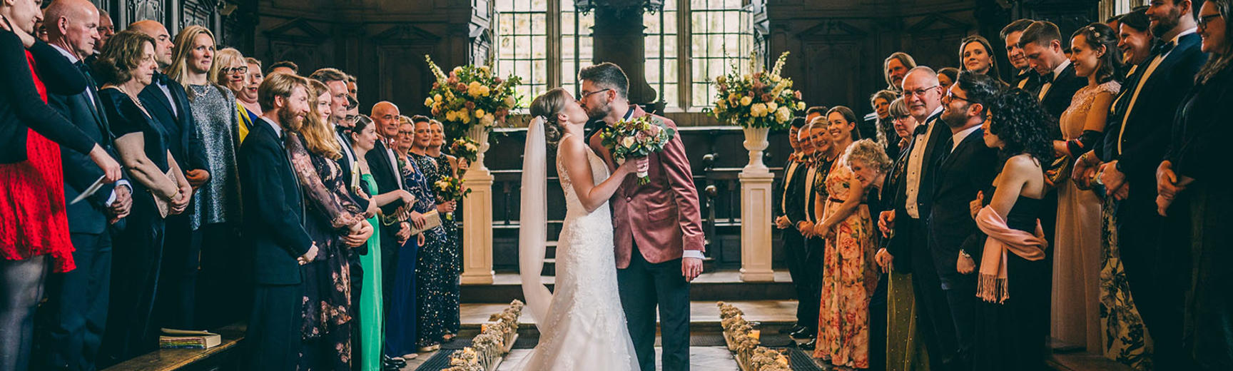 A bride and groom kiss in front of a crowd at their wedding ceremony at the Bodleian Library