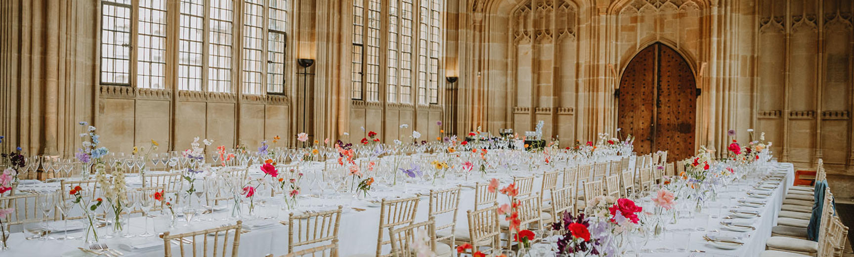 Two long tables laid for a wedding: with a white table cloth and red flowers in vases