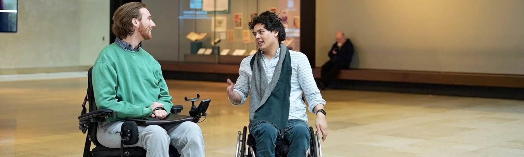 Two people in wheelchairs speak to each other in a large hall