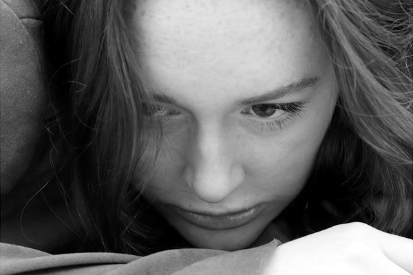 A close up on a woman's face - her eyes are cast down and she rests her chin on her hand
