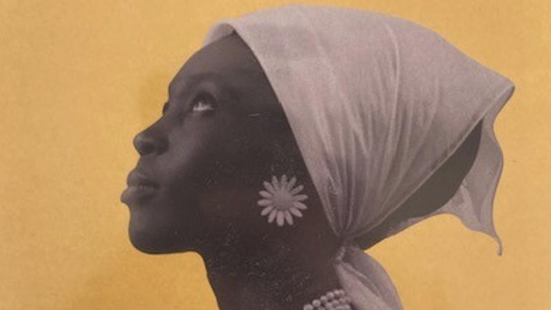 An illustrated face of the side profile of a black woman with a pick headscarf and a large pink earring