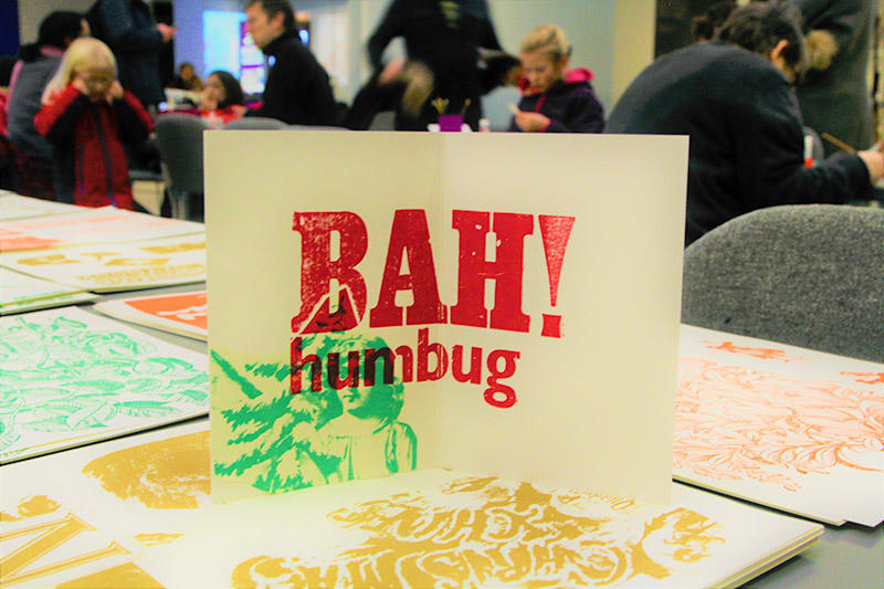 A christmas card with the words 'Bah! Humbug' in block print on a table, surrounded by other printed cards