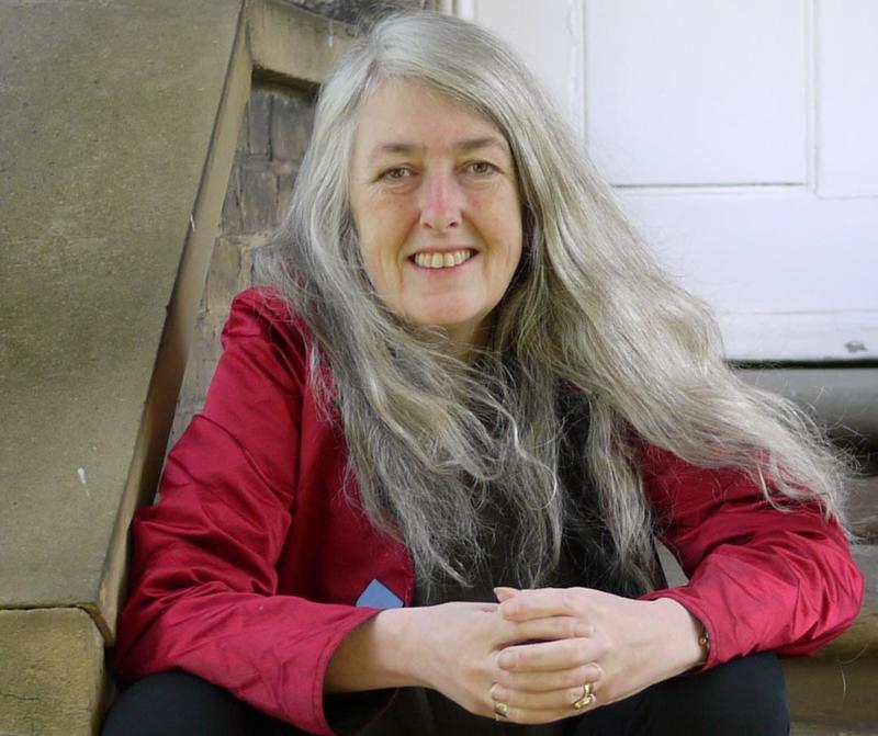 A woman with long silver hair wearing a red top sits on stone steps