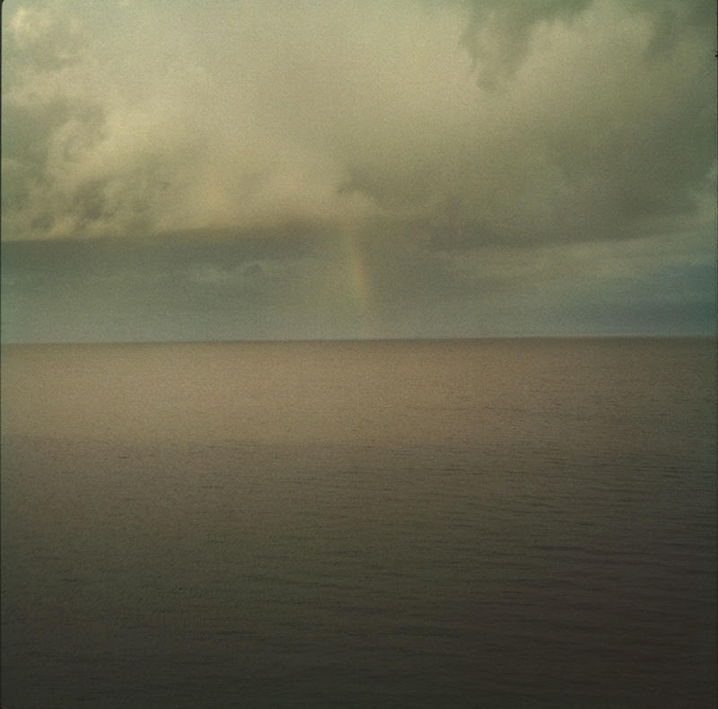 A grey seascape under a grey sky with a rainbow