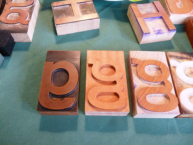 Wooden type-blocks for 'g' and 'h' on a green surface