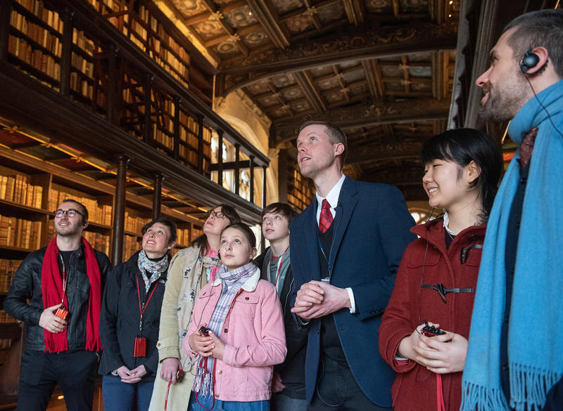 A group of people stand around a tour guide - they are all looking to their left