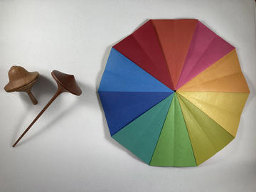 A wooden spinning top next to a colour wheel showing blue, green, yellow, orange, pink and red segments
