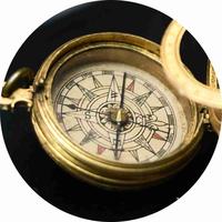The detail of a compass: it is round and gold and the compass points in the centre are different coloured triangles